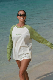 Woman wearing a green and white long-sleeve shirt with 'Bubba's' logo on a beach.