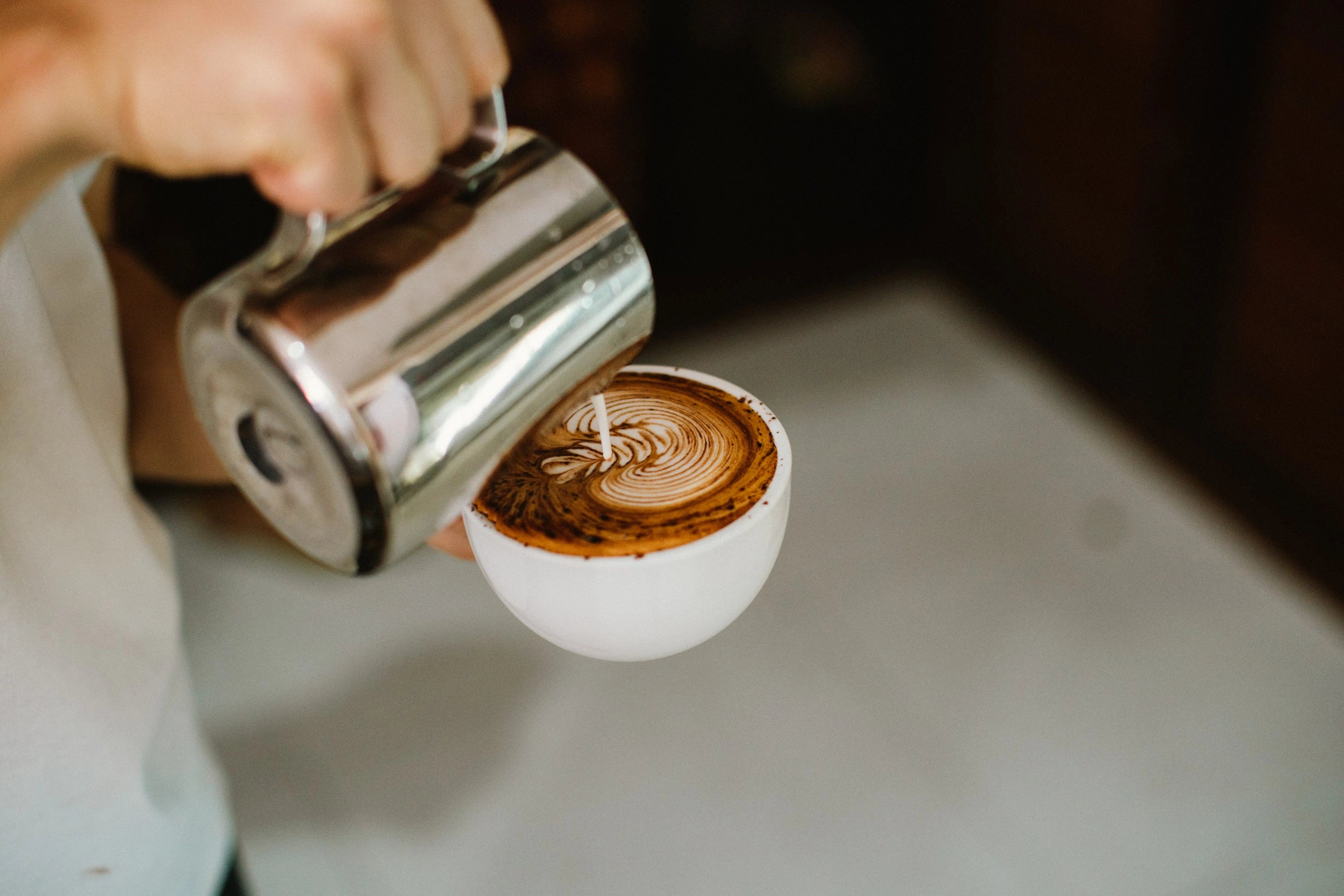Person pouring coffee from a portafilter into a white cup with a latte art design.
