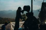 Person operating a large camera on a tripod with mountains in the background.