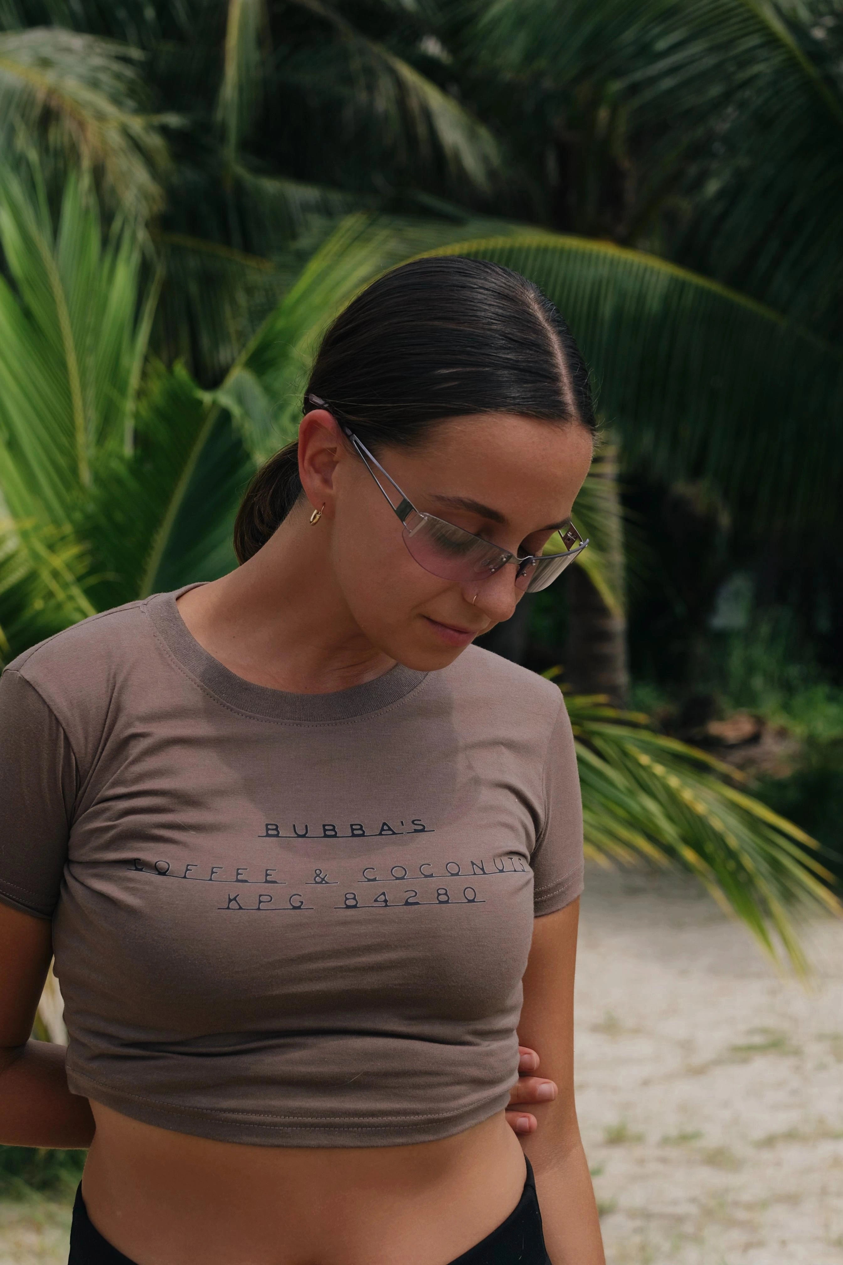 Woman wearing a gray t-shirt with text, standing outdoors with greenery in the background