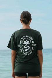 Person wearing a green t-shirt with text and graphics, standing by the ocean.