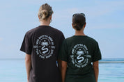 Two people wearing black t-shirts with a palm tree design and text, standing by a body of water.