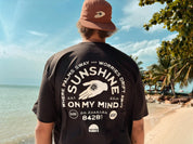 Person wearing a black t-shirt with 'Sunshine on My Mind' design at a beach.
