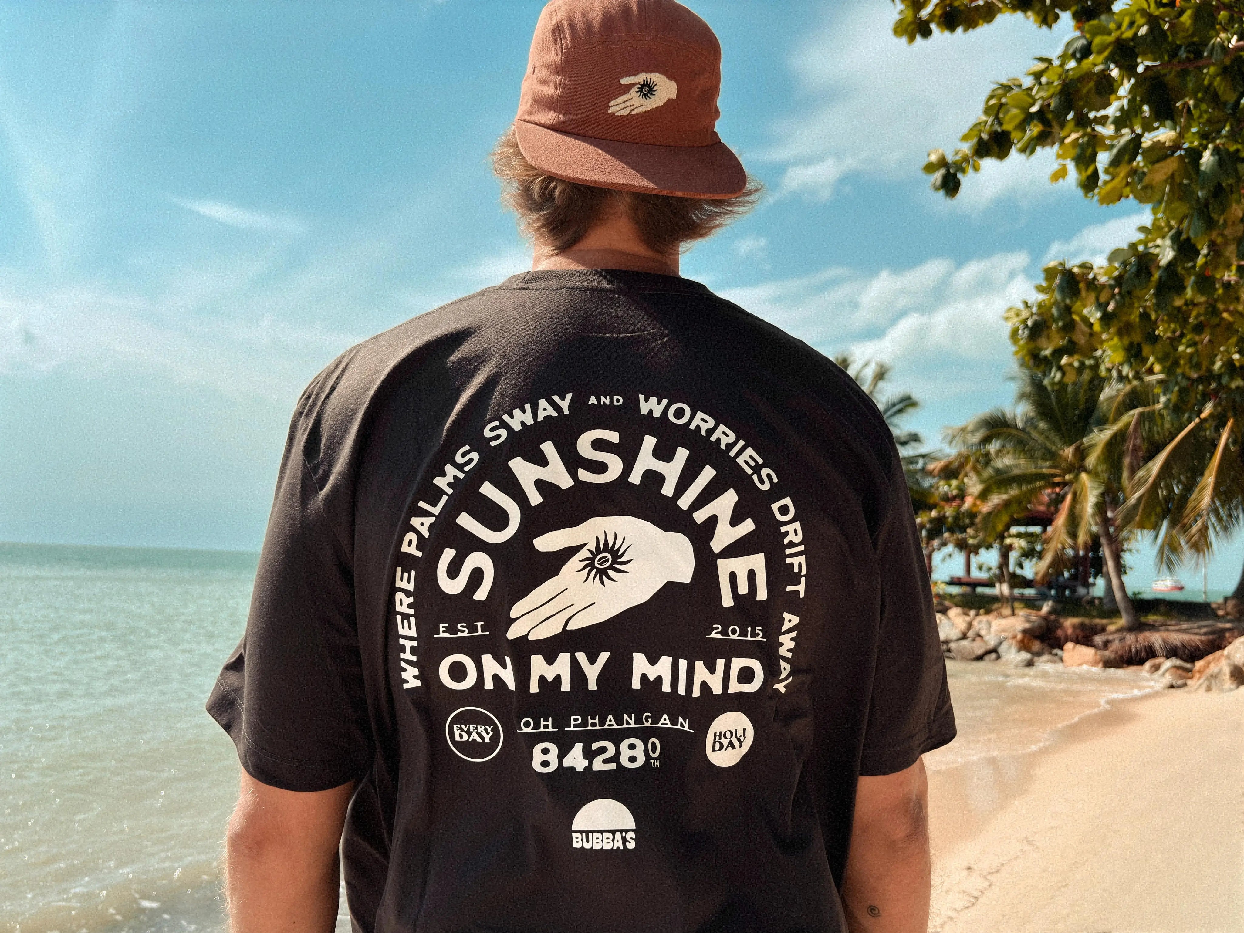 Person wearing a black t-shirt with 'Sunshine on My Mind' design at a beach.
