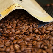 Open bag of coffee beans with a focus on the beans spilling out.