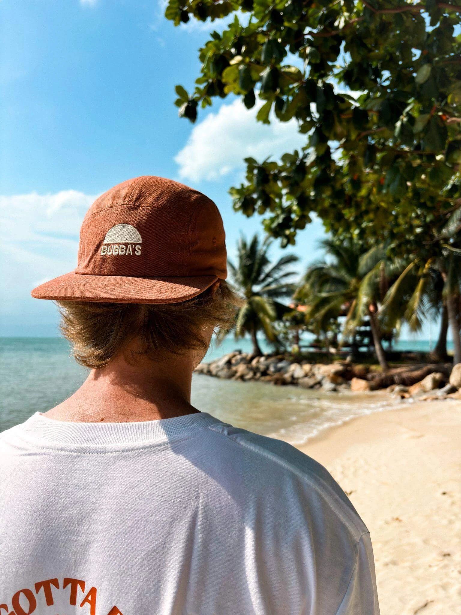 Person wearing a brown cap and white shirt with 'Bugg's' logo, standing on a beach.
